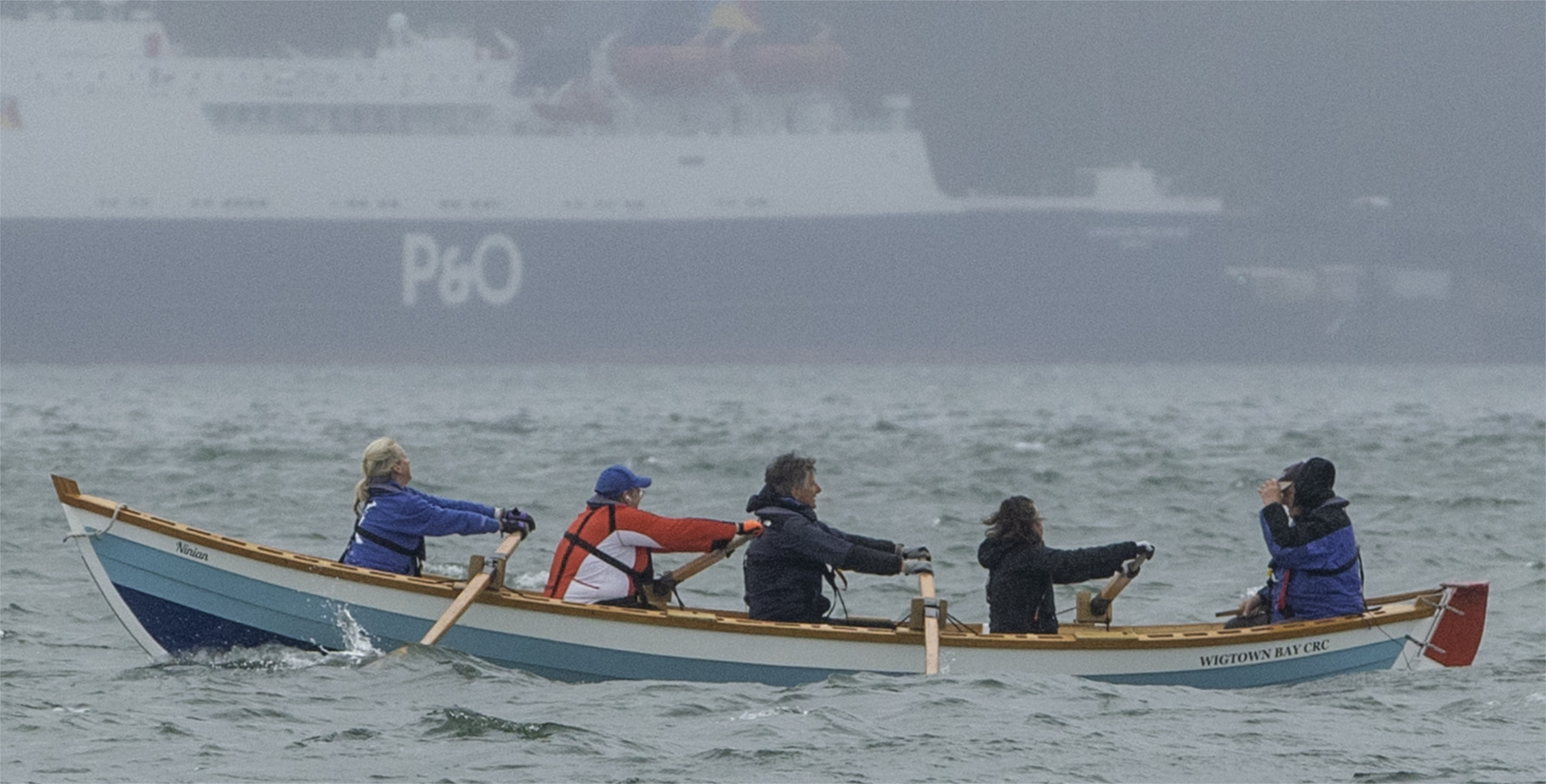 A St Ayles skiff coastal rowing boat with a ferry in the background