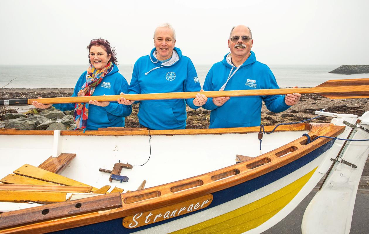 Three people holding an oar while standing next to a skiff boat