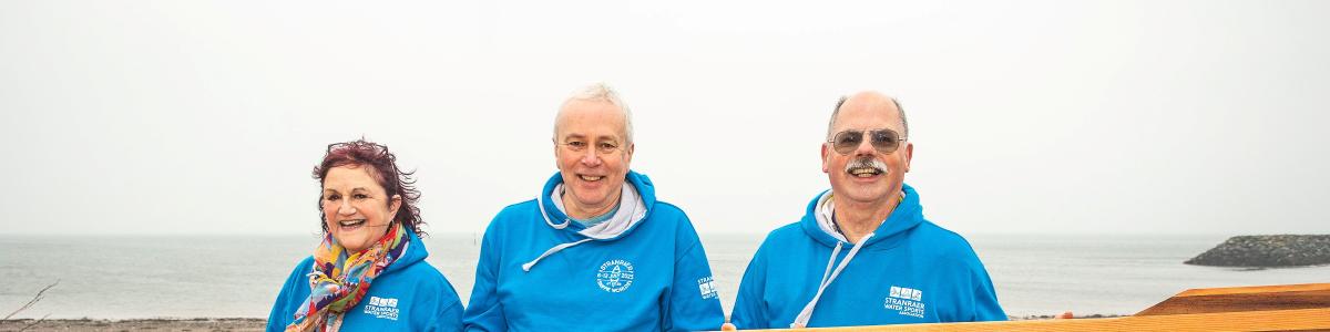 Three people holding an oar alongside a coastal rowing boat